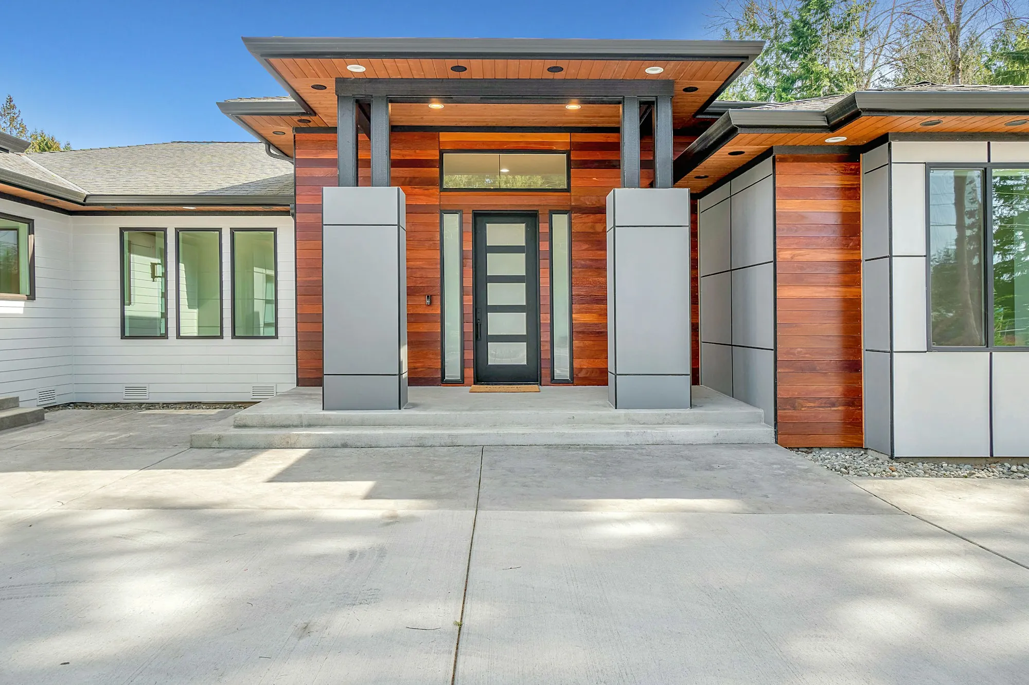 Modern house entry with wood panels and a wide concrete drive
