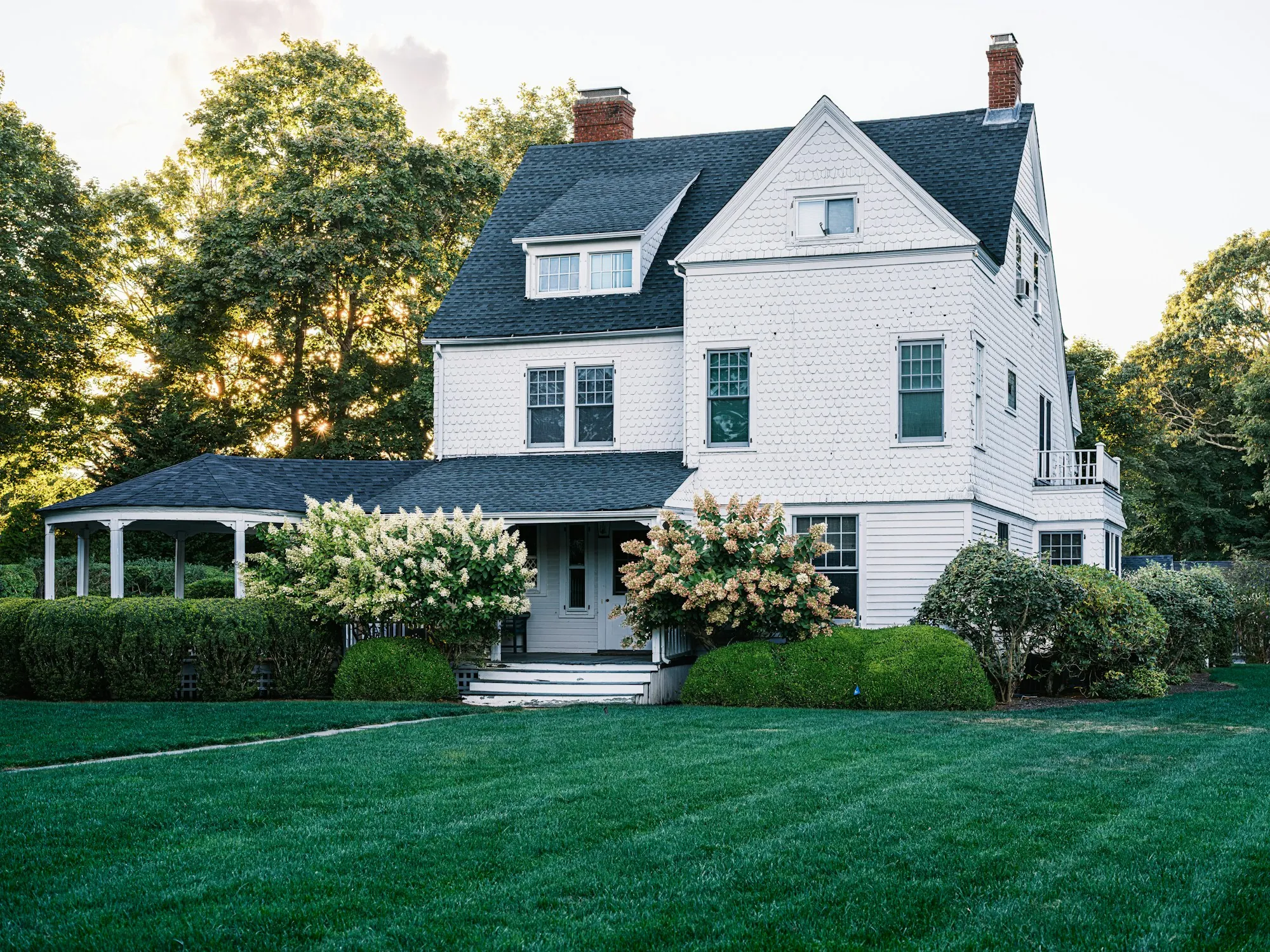 White three-story house with dark roof behind flowering hydrangeas